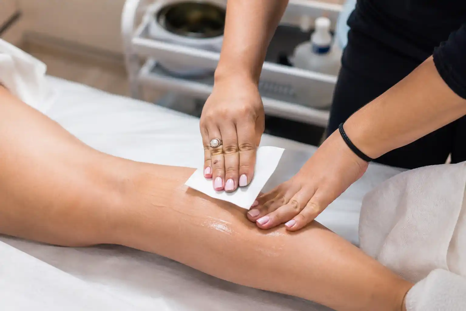 Beautician pressing a wax strip onto a client’s leg during a waxing appointment at home in Jaipur
